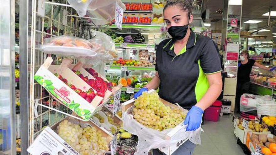 La trabajadora de una frutería coge una caja de uvas blancas en venta para la Nochevieja.