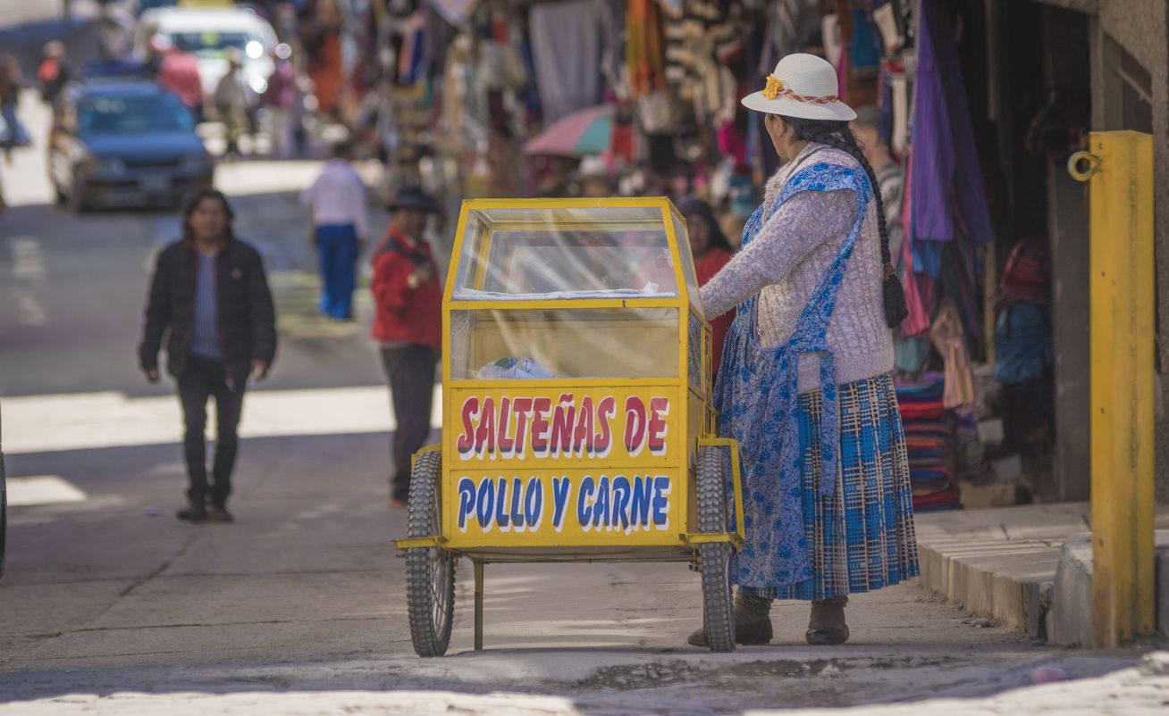 Cholita vendiendo empanadas salteñas en una calle.