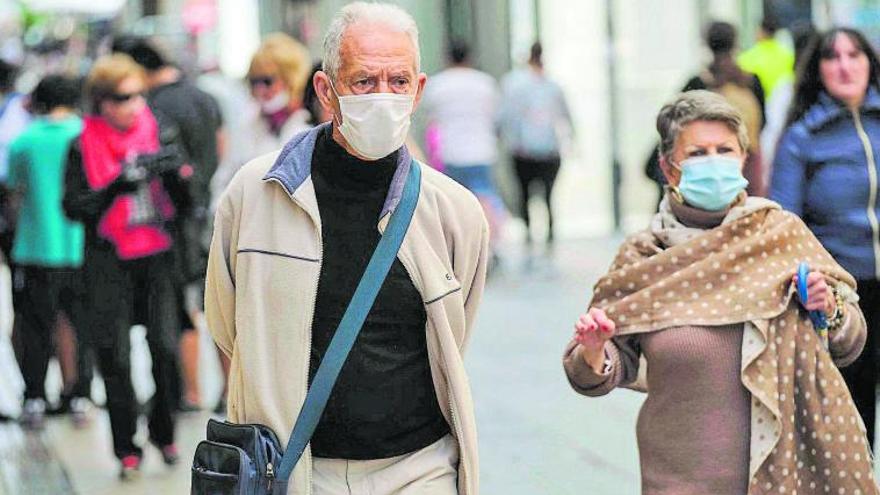 Dos personas pasean por la calle con mascarillas.