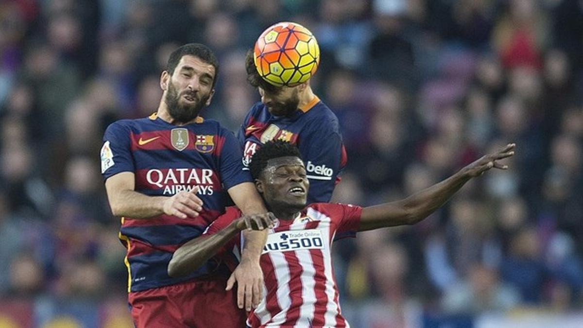 Arda y Piqué se anticipan el el salto a Thomas durante  el partido de liga entre el FC Barcelona y el Atlético de Madrid.
