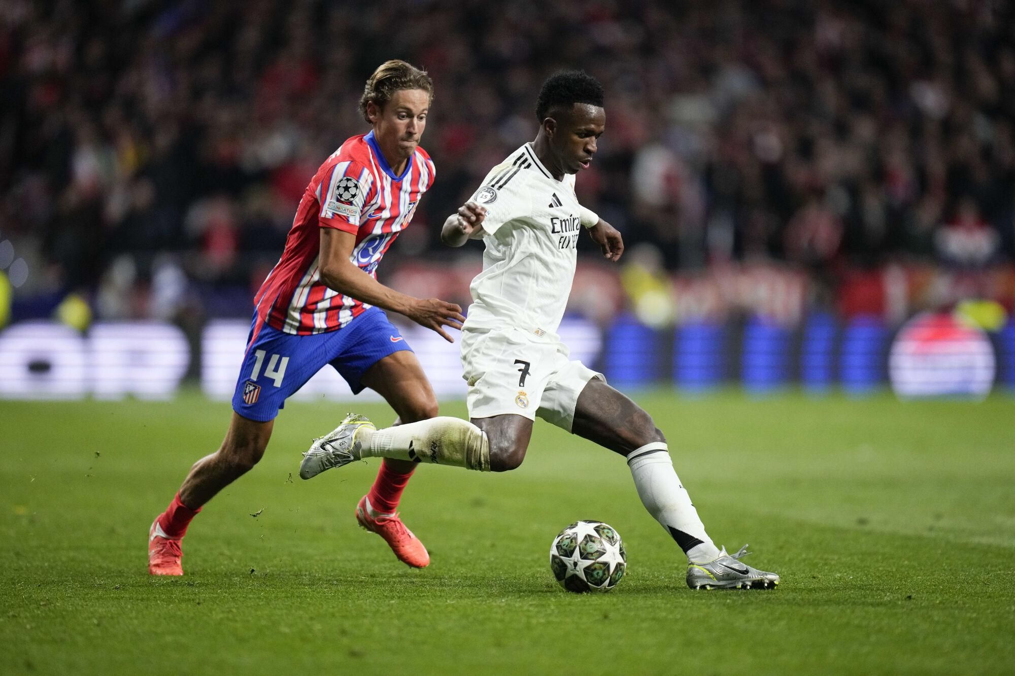 Real Madrid's Vinicius Junior in action in front of Atletico Madrid's Marcos Llorente during the Champions League round of 16, second leg, soccer match between Atletico Madrid and Real Madrid at the Metropolitano stadium in Madrid, Spain, Wednesday, March 12, 2025. (AP Photo/Bernat Armangue). EDITORIAL USE ONLY/ONLY ITALY AND SPAIN