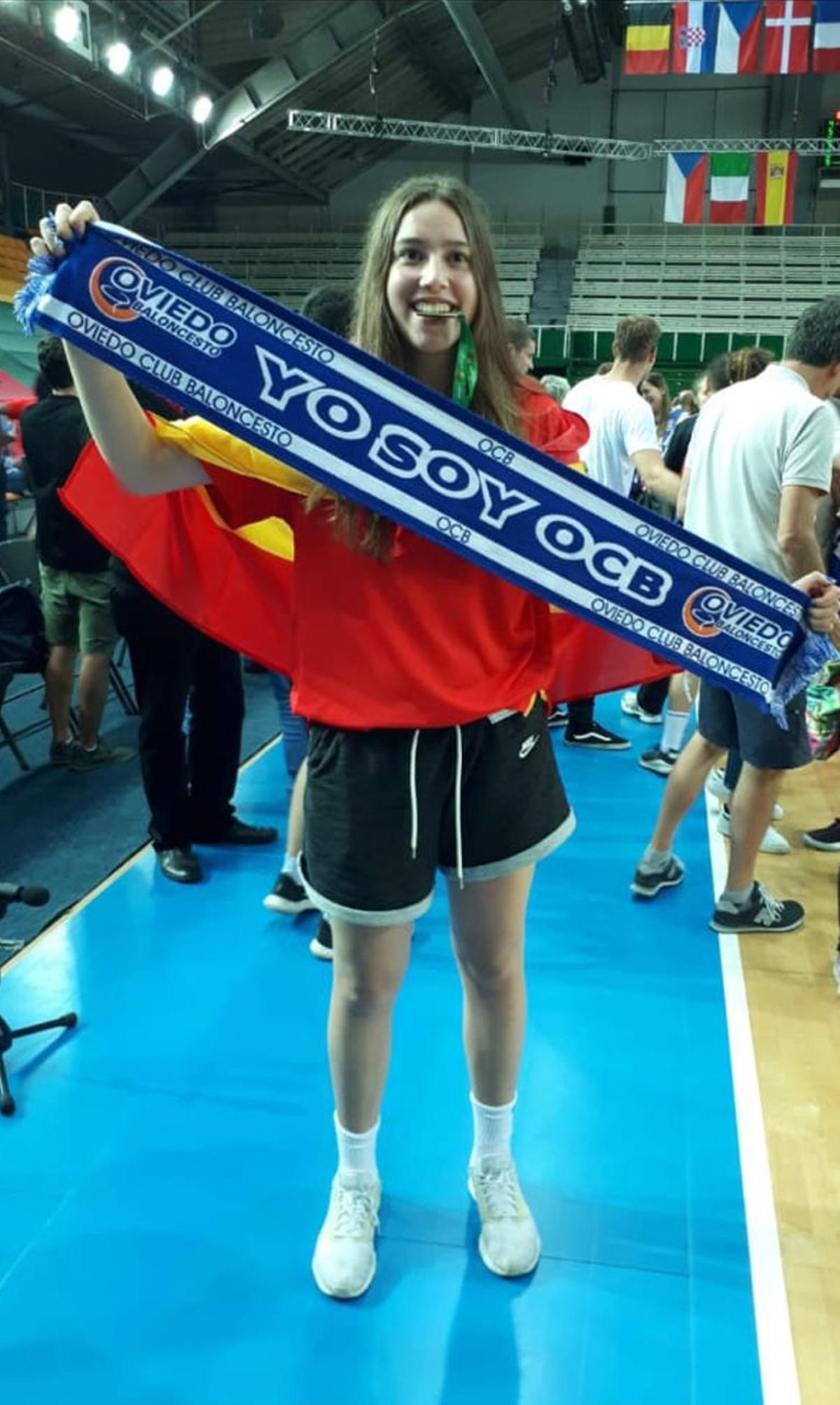 La jugadora, muy joven, muestra orgullosa una bufanda de su equipo de formación, el Oviedo Baloncesto.