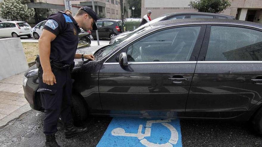 Un agente supervisa la tarjeta de un vehículo estacionado en una plaza para discapacitados. // FdV