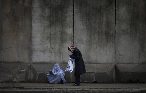 A woman stops to give money to beggar wearing burqa outside a police station in Kabul