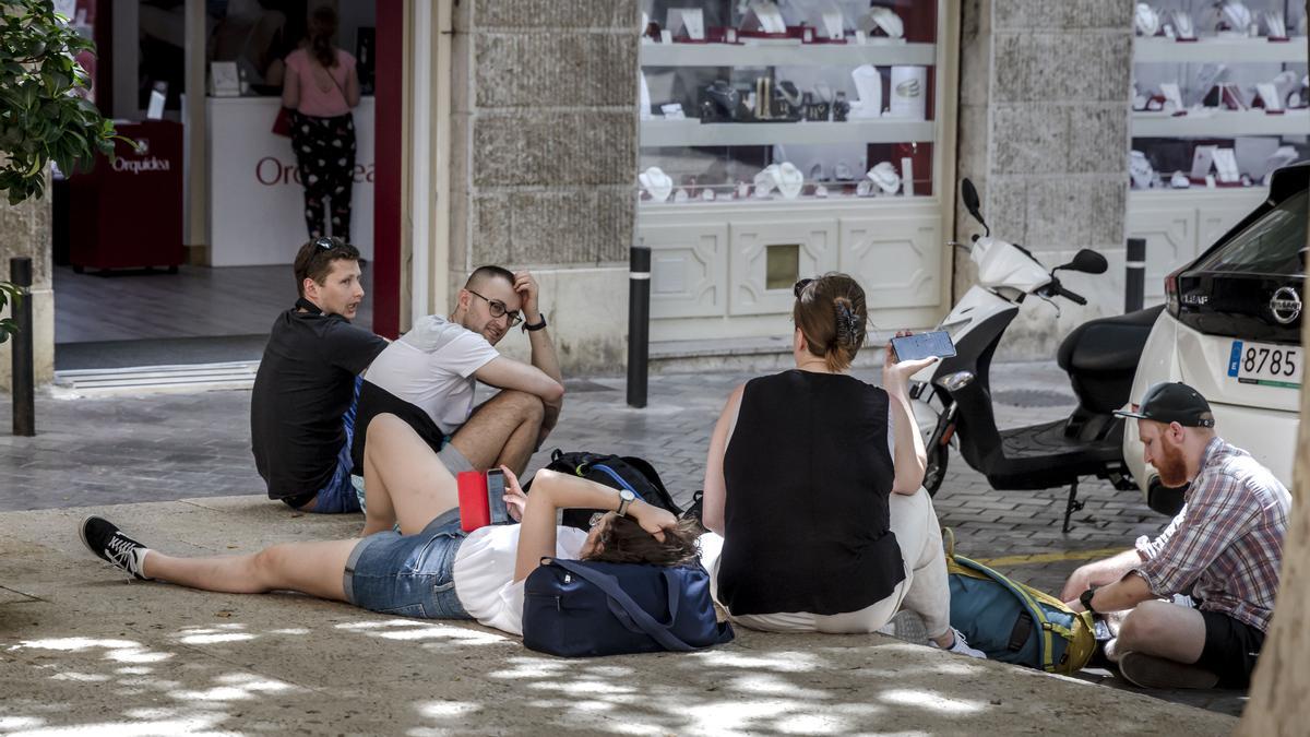 Unos turistas, sentados en una sombra de Palma, recuperan el aliento en un día de temperaturas extremas