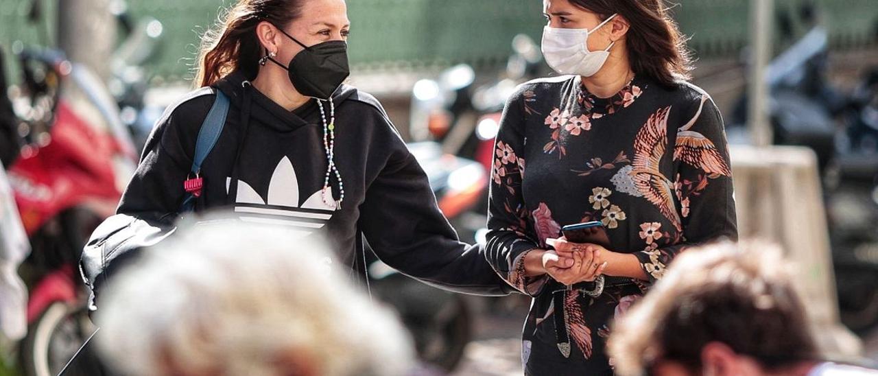 Dos mujeres pasean charlando bajo la protección de sus mascarillas.