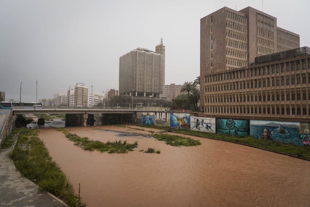 El río Guadalmedina crecido con agua y calles del Centro y el entorno del cauce, desiertas bajo la lluvia, la estampa de este martes 31 de marzo.