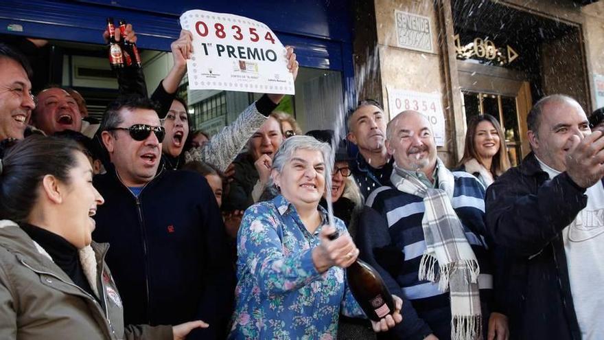 Vecinos de Torrent (Valencia) celebran ante la administración de lotería el primer premio del sorteo del Niño. Abajo, Amparo Masilla, propietaria de la administración de lotería.