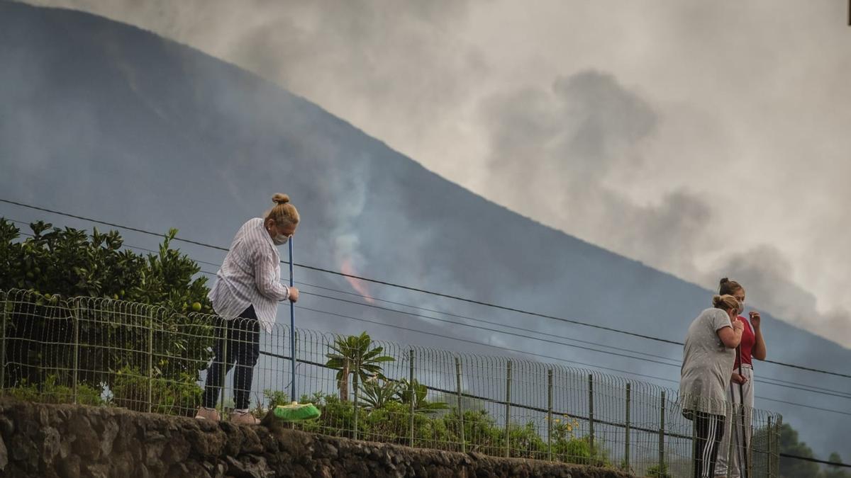 Dos vecinas retiran cenizas volcánicas después de abrirse una nueva boca en el volcán de La Palma.