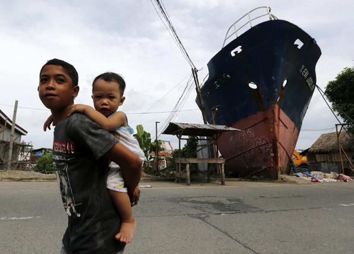 Dos nens filipins passen davant d’un vaixell de càrrega que va acabar encallat al poble d’Anibong durant el tifó Haiyan que va arrasar el país el 2013, a la ciutat de Tacloban.