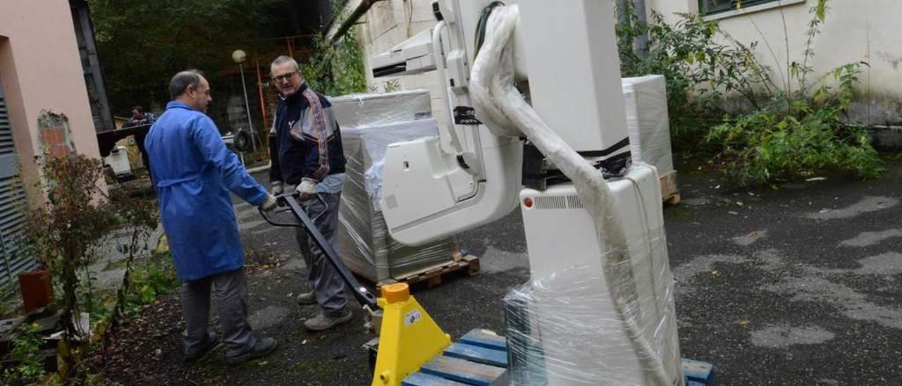 Dos operarios, en el exterior del viejo hospital, trasladando un equipo médico.