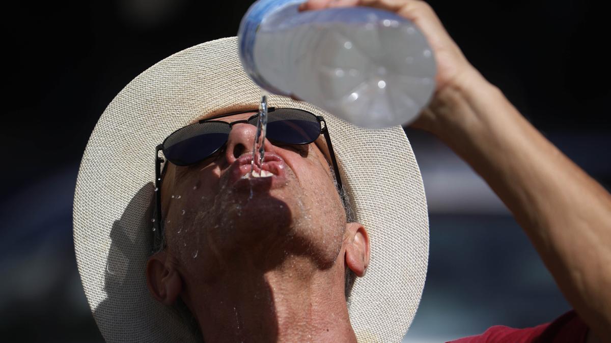 Un hombre se refresca con agua de una botella mientras camina por el Puente Romano de Córdoba.