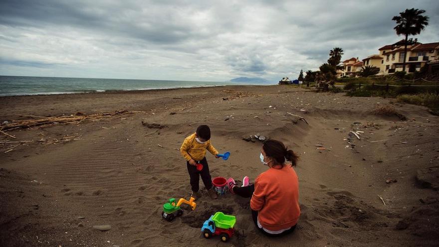 Una mujer y su hijo, ambos con mascarillas, juegan en la playa de Torre de Benagalbón.