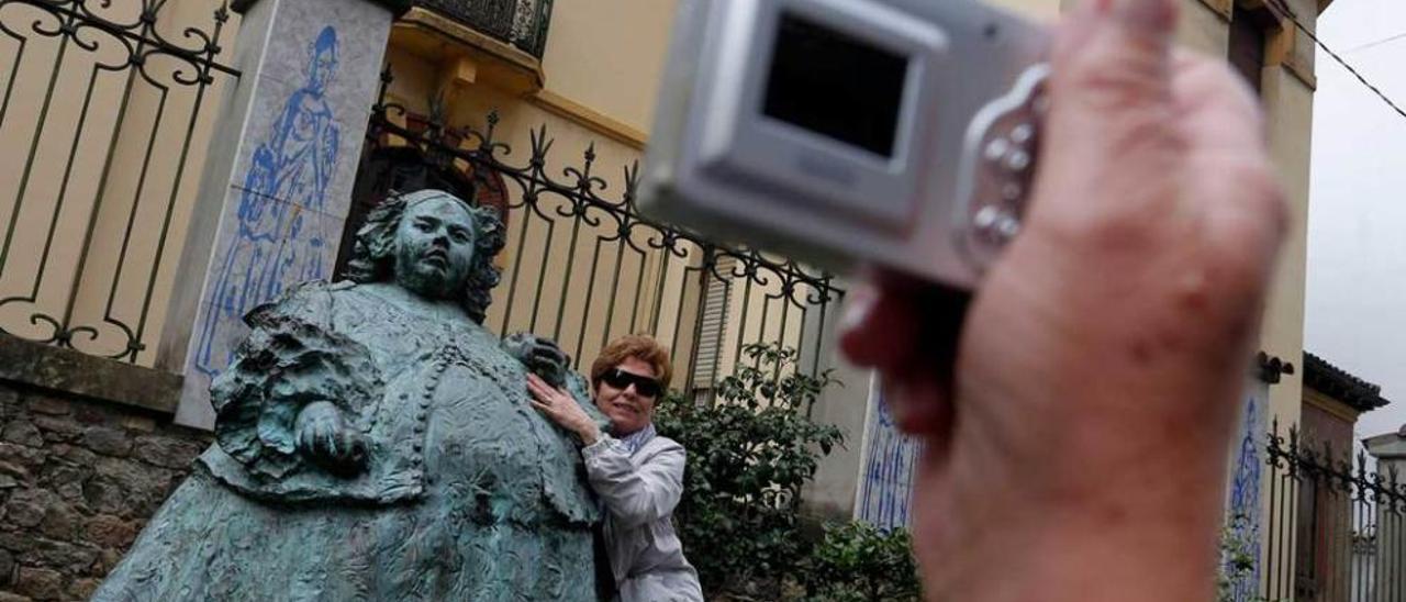 Una turista se fotografía junto a la escultura de &quot;La Monstrua&quot;, en la calle Carreño Miranda. A la derecha, un grupo de turistas desde la capilla de Las Alas.