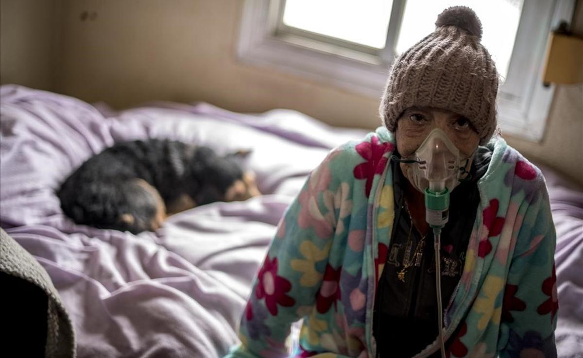 Carmen, sentada en una esquina de la cama conectada al respirador, acompañada por su perra Linda en su casa en el barrio de Torre Baro.