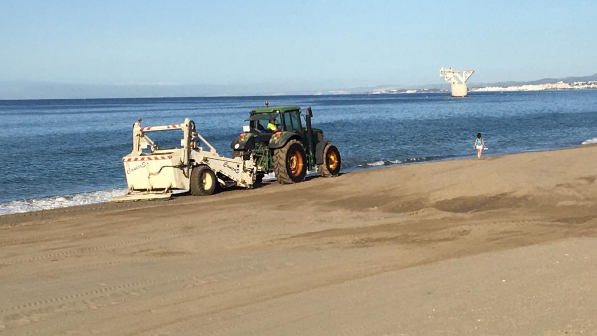 Un tractor extiende arena en la orilla de una de las playas de Marbella